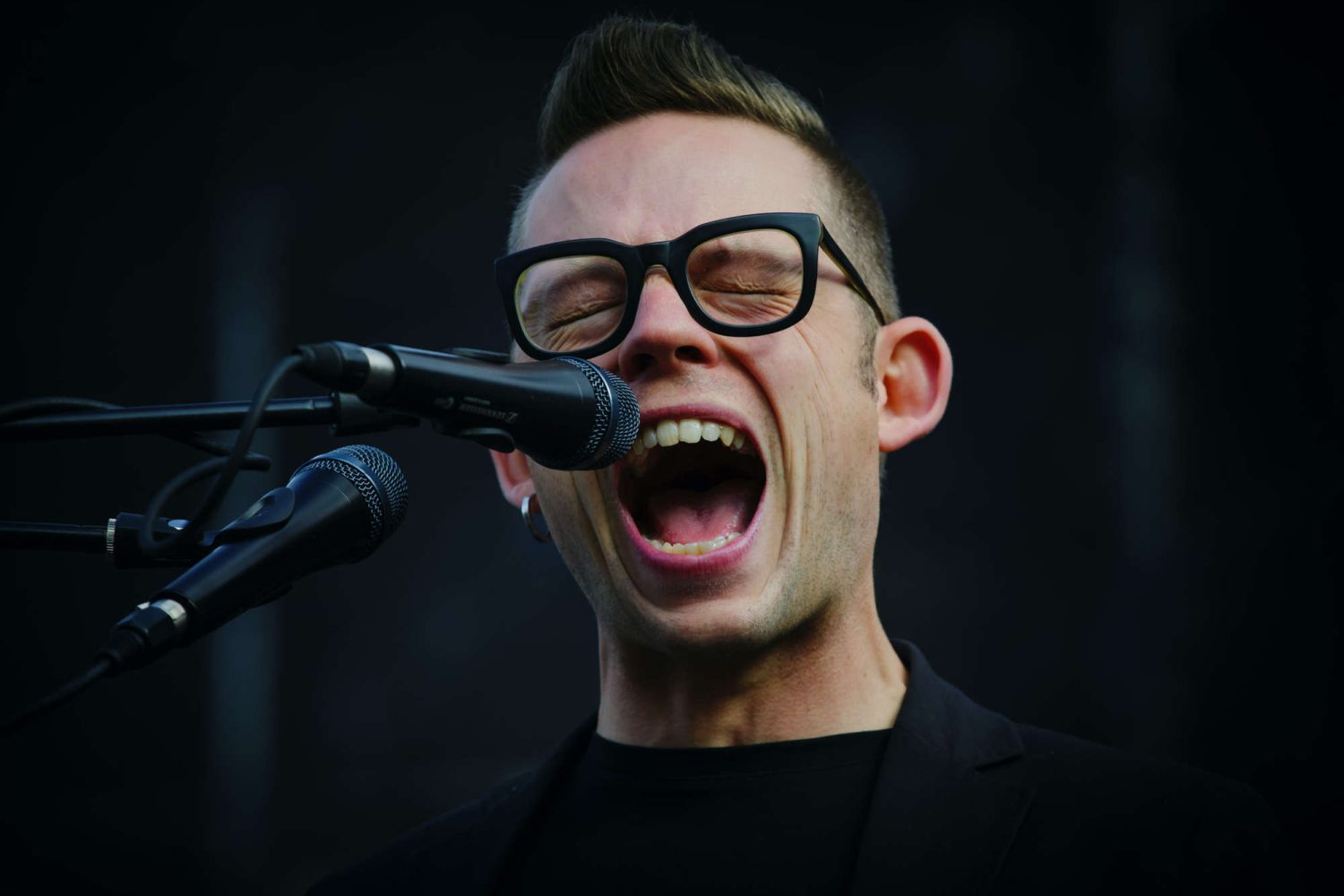 Sänger mit Brille und geschlossenen Augen mit Mikrofon, am hoch singen aus vollem Halse